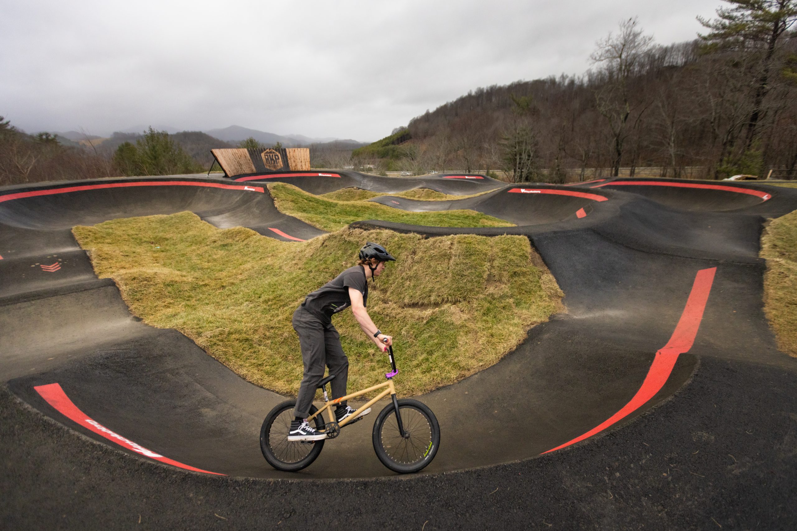 A rider wearing a black shirt and grey pants rides a yellow mountain bike on the new pump track at Rocky Knob Park